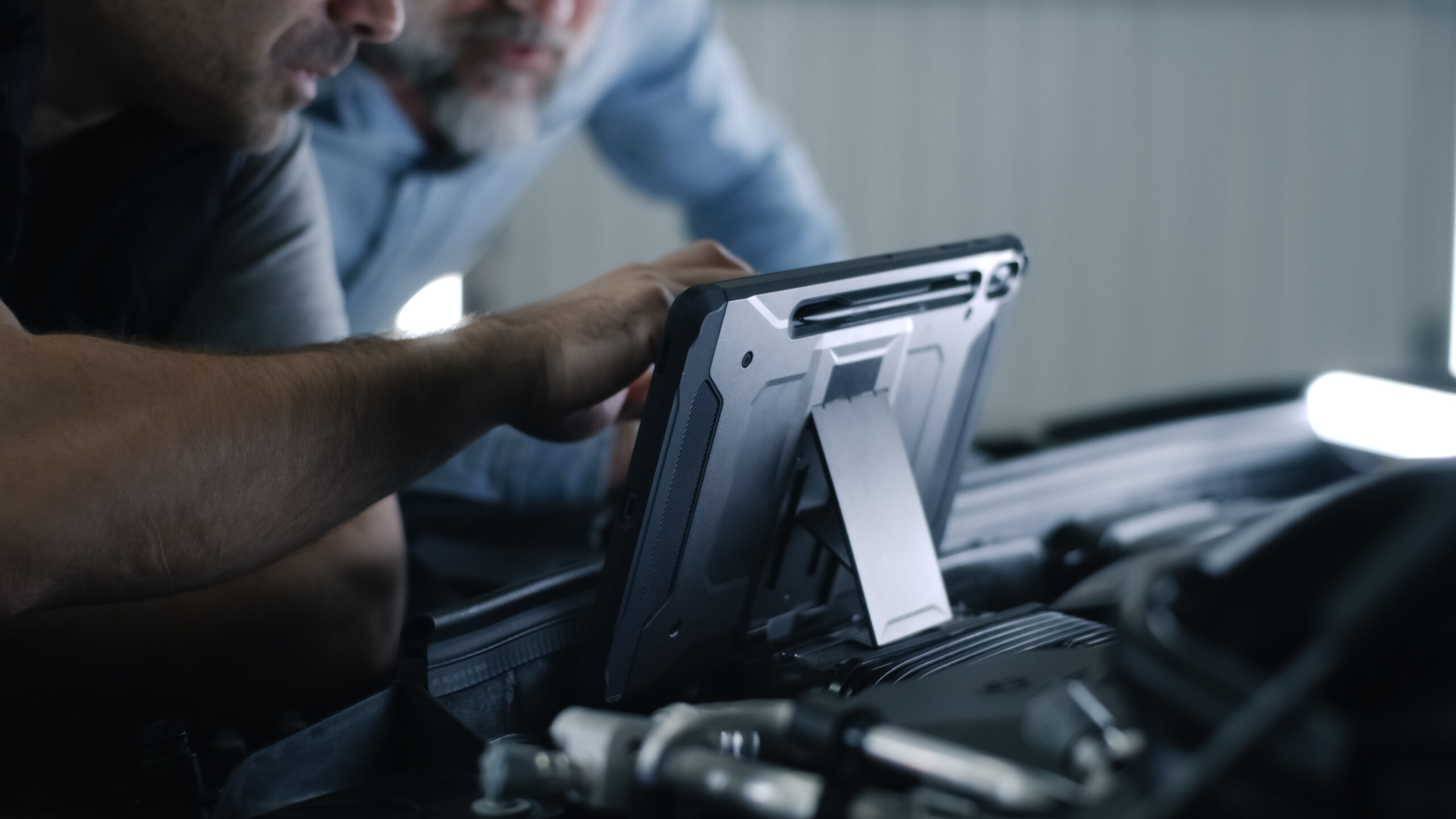 Car mechanic with client using tablet Car service mechanic clicking on a screen of digital tablet computer while standing next to a client, near the opened bonnet of the car during diagnostics and maintenance